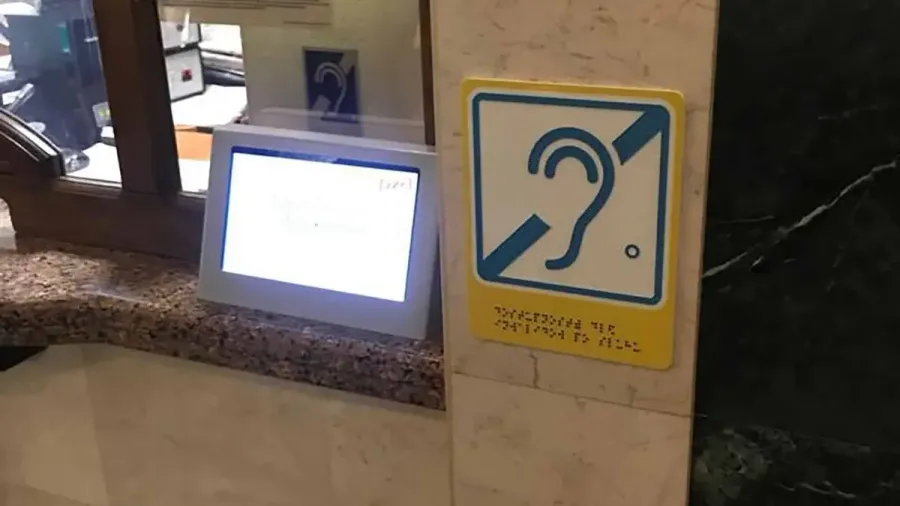 Panel de información con el pictograma de accesibilidad auditiva y texto en braille en una estación