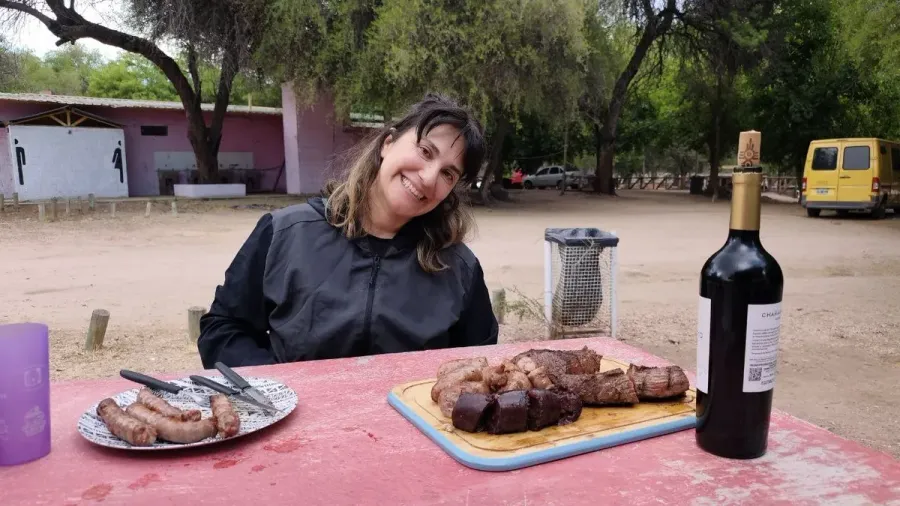 Cris sonríe en una mesa del camping de Andolucas, con una tabla de asado y una botella de vino tinto delante