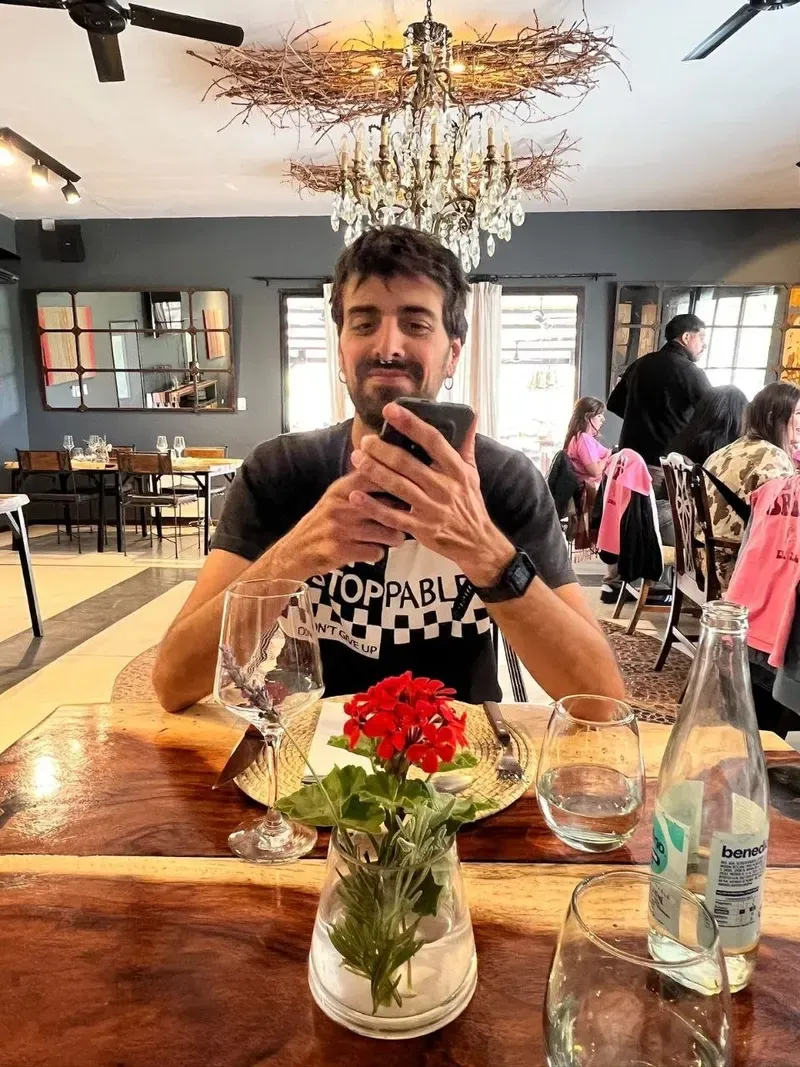 Sergi sentado a la mesa del comedor de la bodega, con una flor roja en un jarrón y una lámpara de ramas colgando del techo