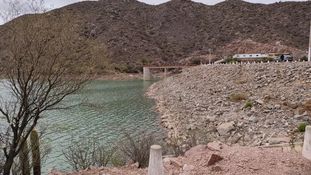 Embalse del dique de Chañarmuyo, de agua verdosa, rodeado de cerros, con el muro y un puente metálico