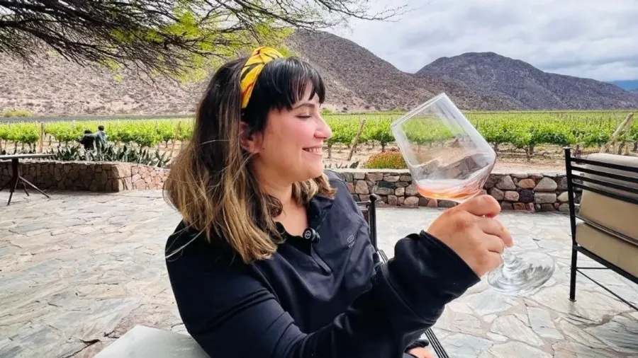 Cris sonríe con una copa de rosado en la terraza de piedra de la bodega Chañarmuyo, con viñedos y montañas detrás