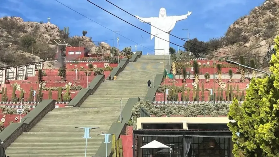Escalinata de cemento y terrazas rojas con cactus que suben hasta la estatua blanca del Cristo del Portezuelo, en Chilecito