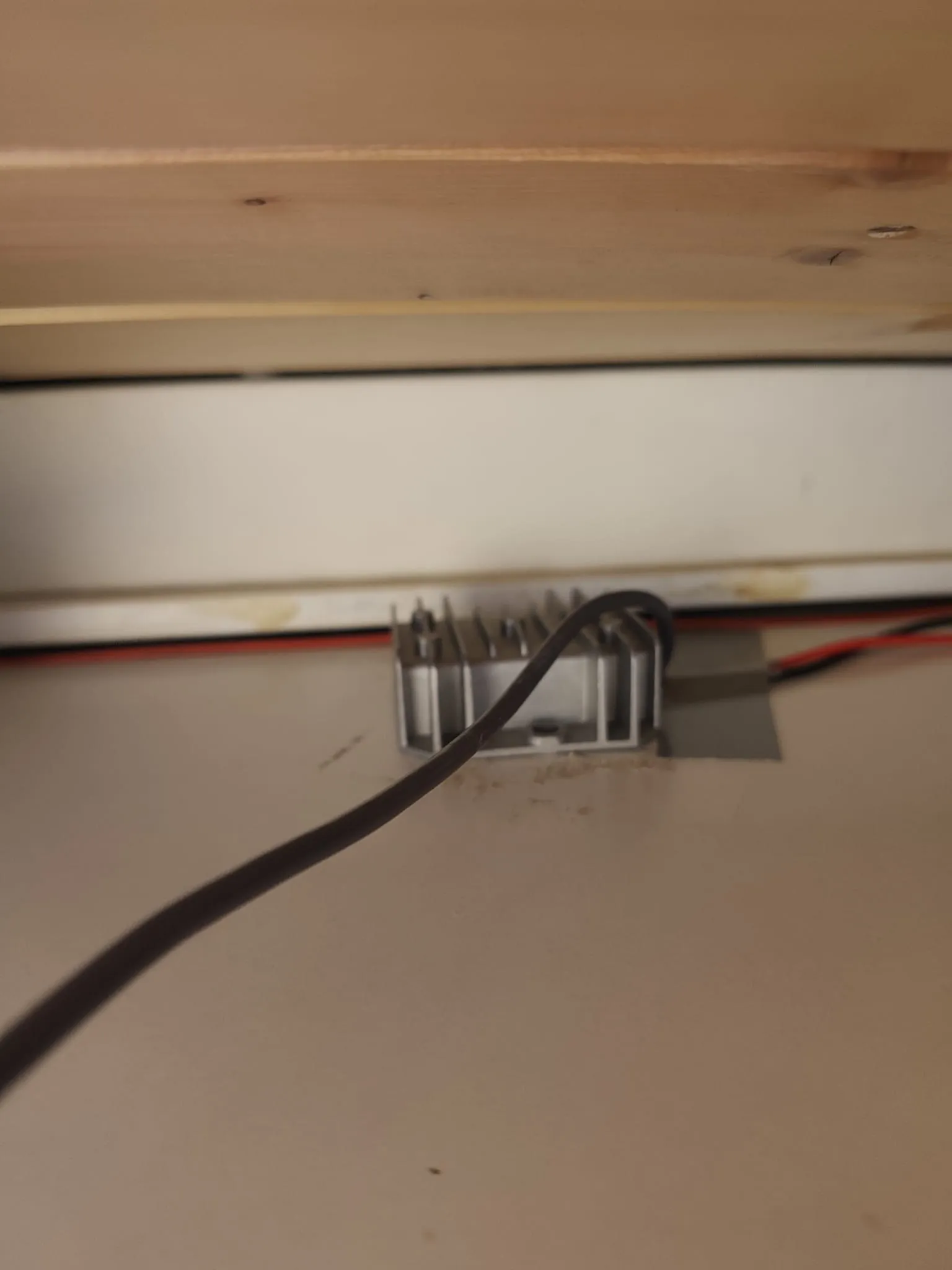 Convertidor de tensión de aluminio con disipador, atornillado bajo un mueble de la camper, con cables rojo y negro de entrada y un cable negro de salida hacia la antena