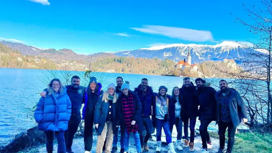 Un grupo de viajeros posando junto al lago Bled, con la isla y su iglesia y los Alpes Julianos nevados al fondo