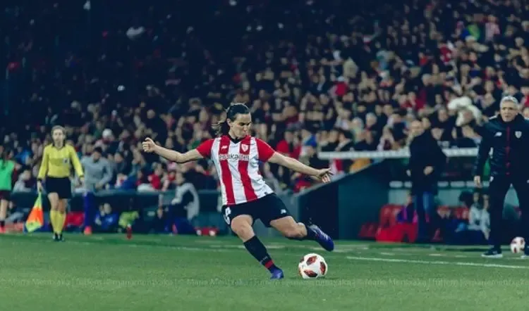 Jugadora de fútbol con la camiseta del Athletic golpeando el balón en un estadio lleno