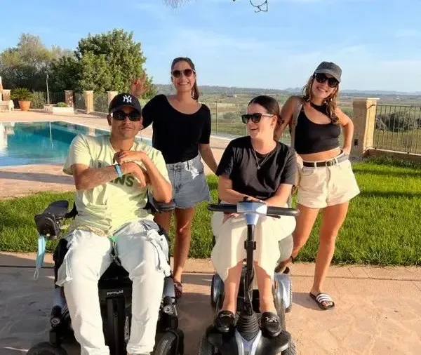 Cuatro personas junto a una piscina, dos de ellas usuarias de silla de ruedas y scooter