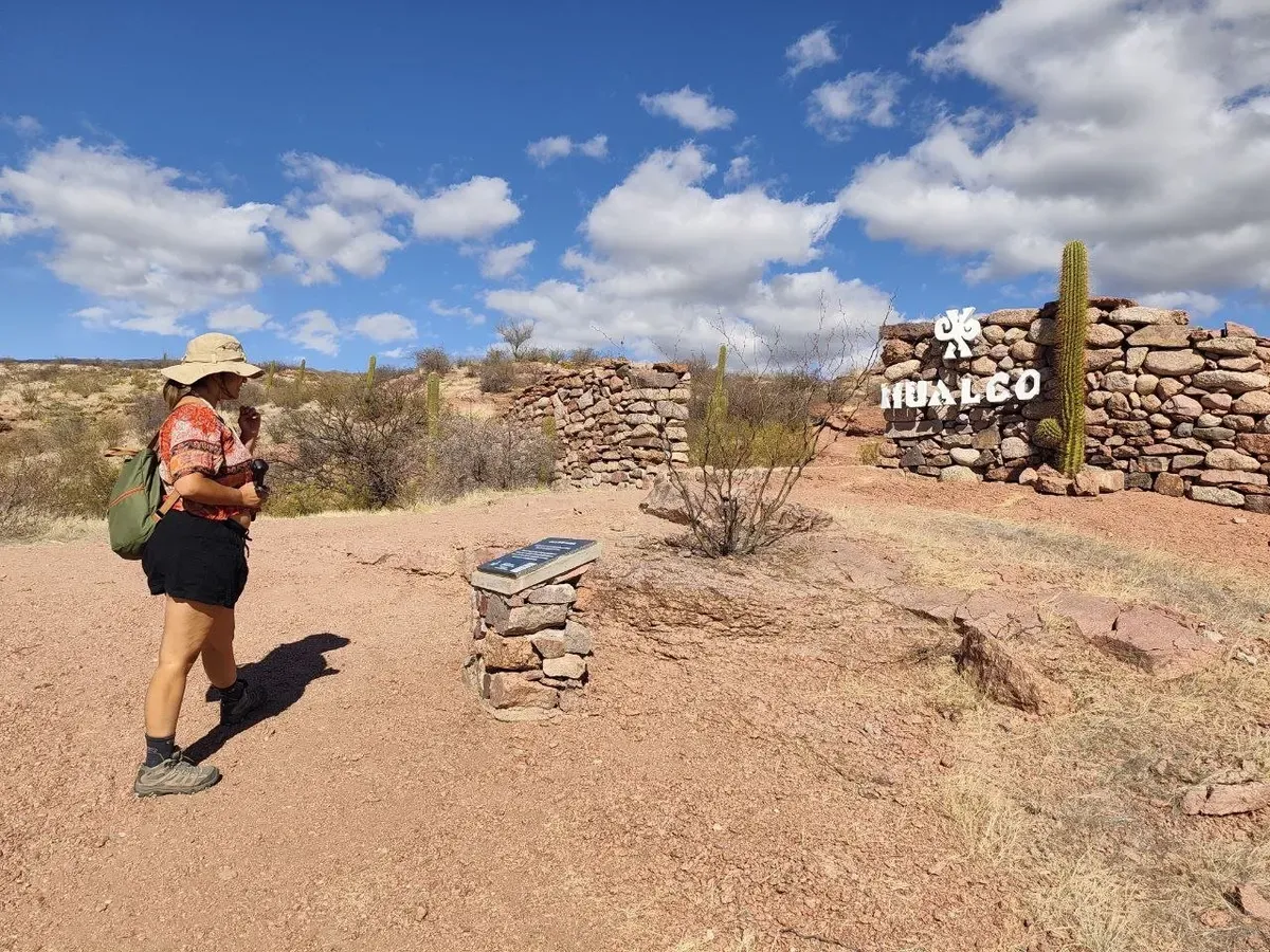 Cris caminando entre los muros de piedra de Hualco, con un cardón detrás