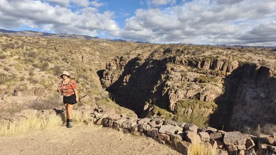 Cris con sombrero al borde de la quebrada de Hualco, con un muro bajo de piedra y las paredes del cañón detrás