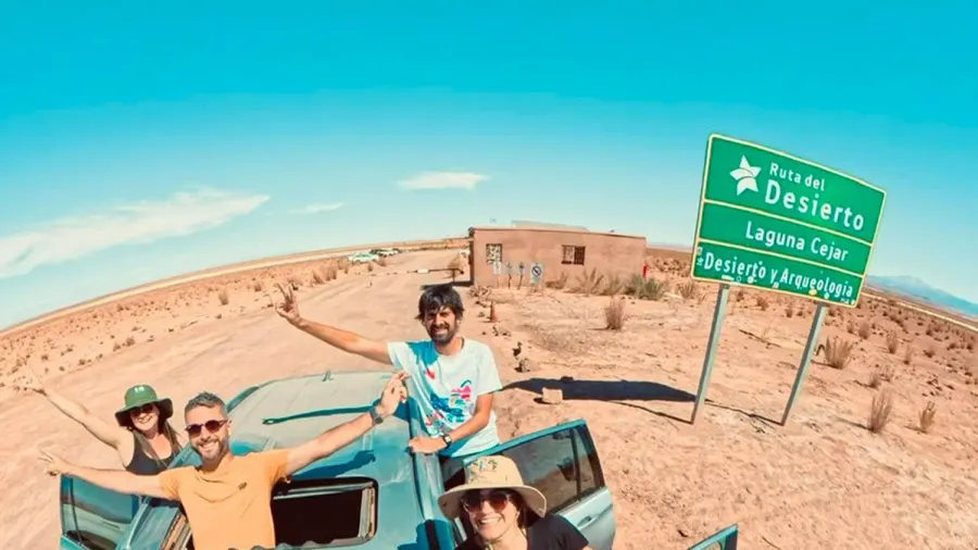 Cuatro viajeros asomados a un coche de alquiler junto al cartel de la Ruta del Desierto que indica Laguna Cejar