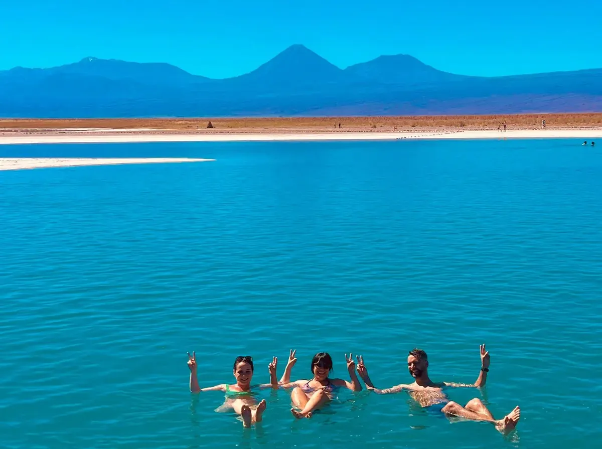 Tres viajeros flotando en las aguas turquesas de la Laguna Cejar, con volcanes al fondo