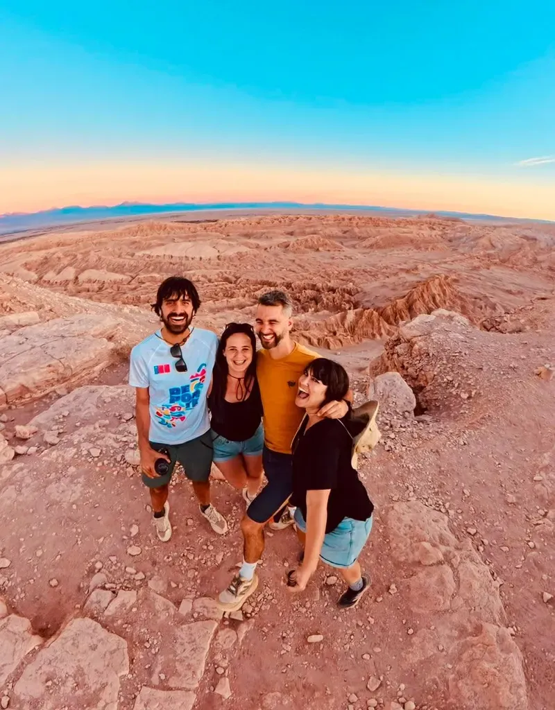 Cuatro viajeros abrazados en un mirador del Valle de la Luna, con el desierto de fondo y el cielo al atardecer