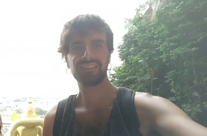 Sergio sonriendo a cámara con el sudor del viaje, con vegetación y una estatua dorada al fondo