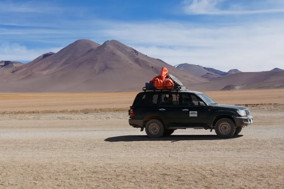 Todoterreno negro con el equipaje en la baca recorriendo el altiplano boliviano entre volcanes