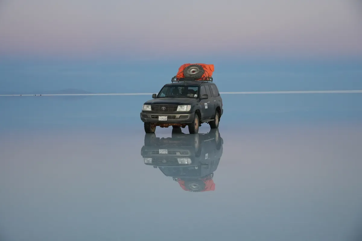 Todoterreno reflejado en el agua del Salar de Uyuni al amanecer