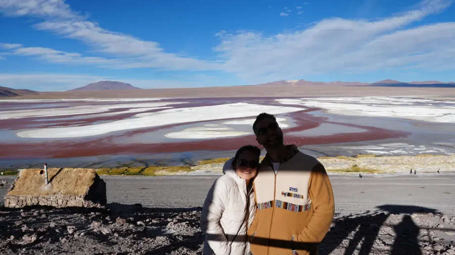 Pareja de viajeros abrazados frente a la Laguna Colorada, con aguas rojizas y bancos de sal blanca, a más de 4.000 metros de altitud