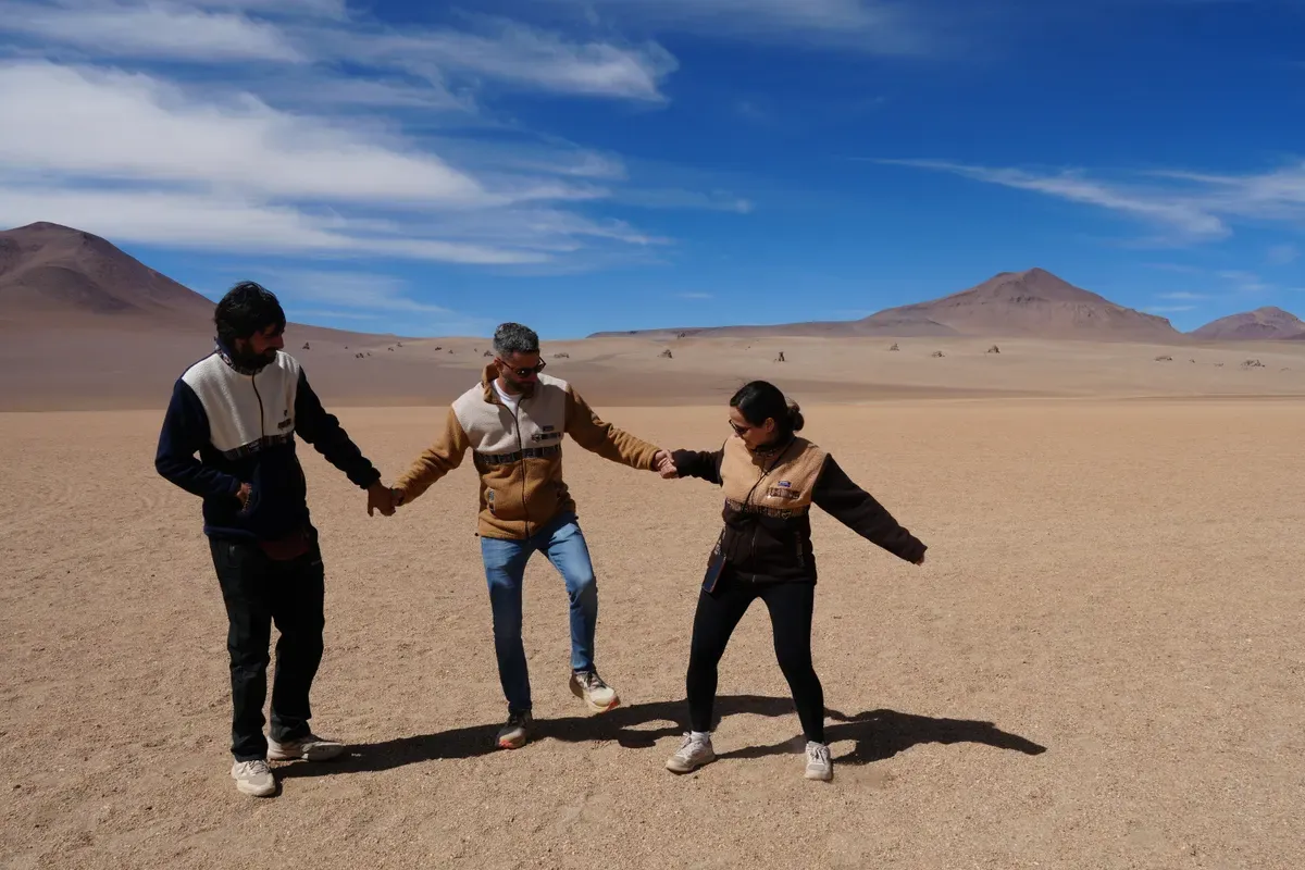 Tres viajeros cogidos de la mano en el desierto del altiplano boliviano, con volcanes y un cielo azul al fondo