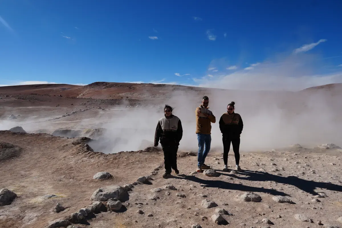 Tres viajeros caminando entre las fumarolas del campo geotérmico del altiplano