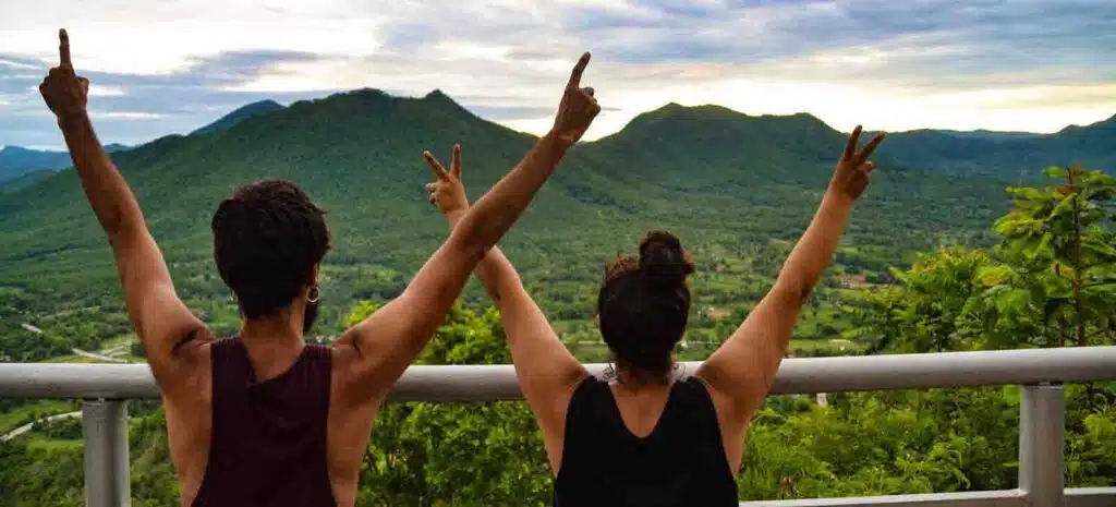 Cris y Sergio foto de espalda, brazos levantados en frente de un un paisaje montañoso, foto destacada