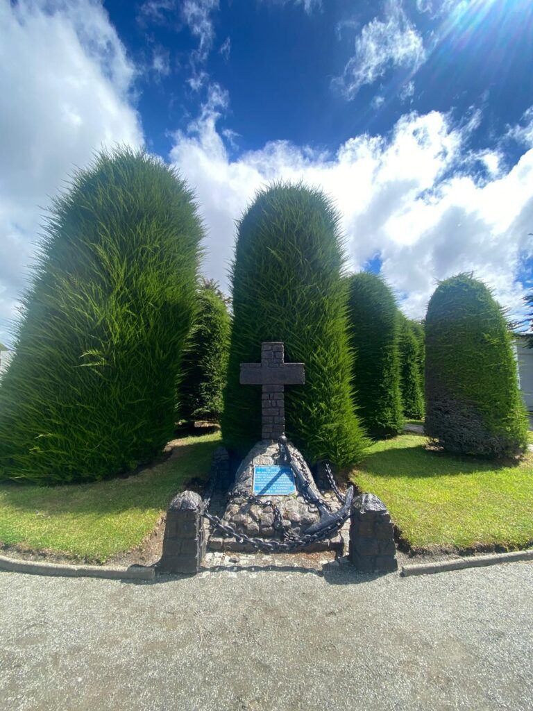 tumba con cruz y detras jardin y arboles 