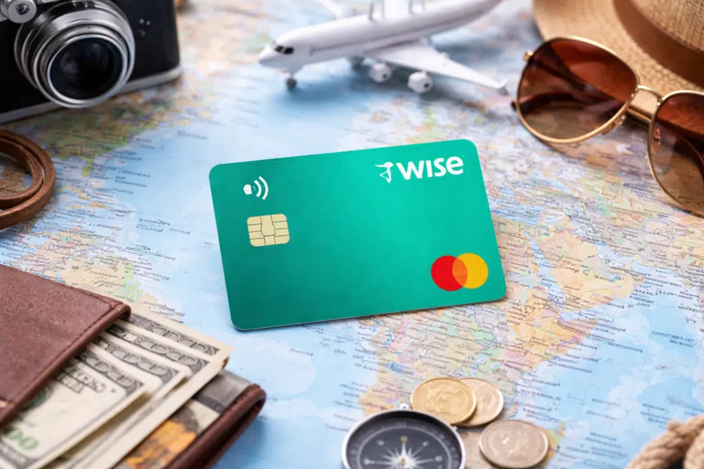 Tarjeta Wise sobre mapa del mundo con dinero, cámara y accesorios de viaje